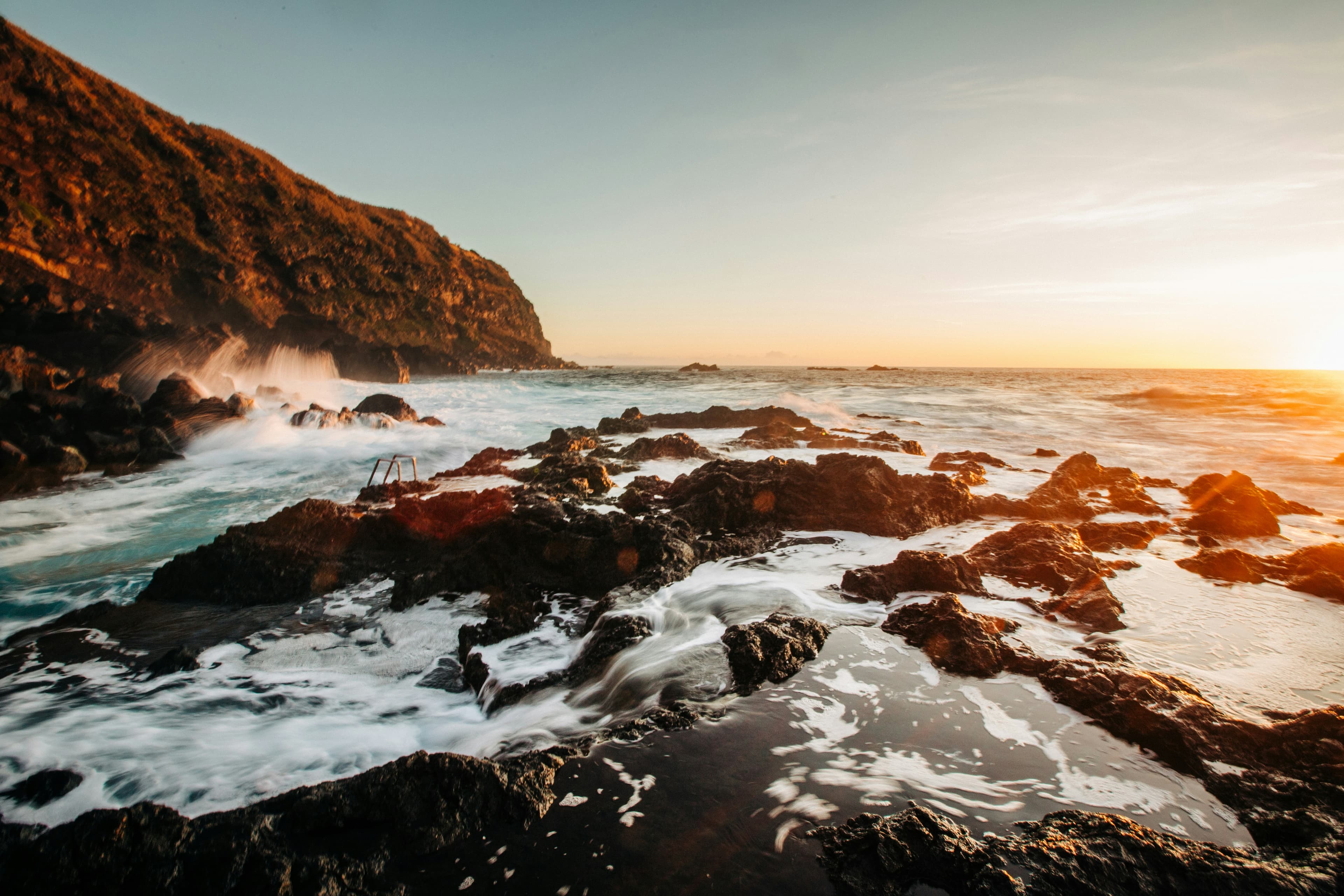 Waves breaking over volcanic rocks on the Azores coastline at sunset
